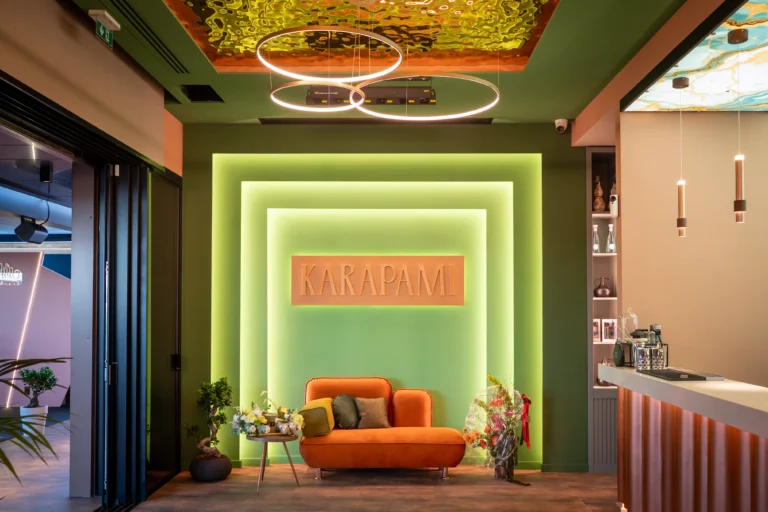 Corner lounge con divano arancione e insegna Karapami retroilluminata, angolo fotografico della sala feste di Giugliano